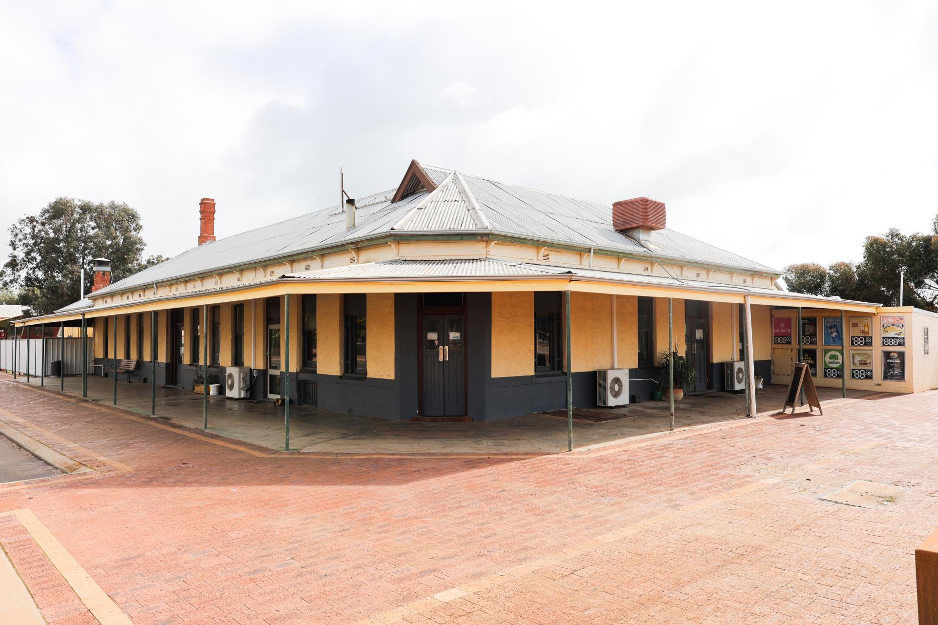 A historic building with a yellow exterior, a corrugated roof, and a covered porch, situated on a brick-paved street.